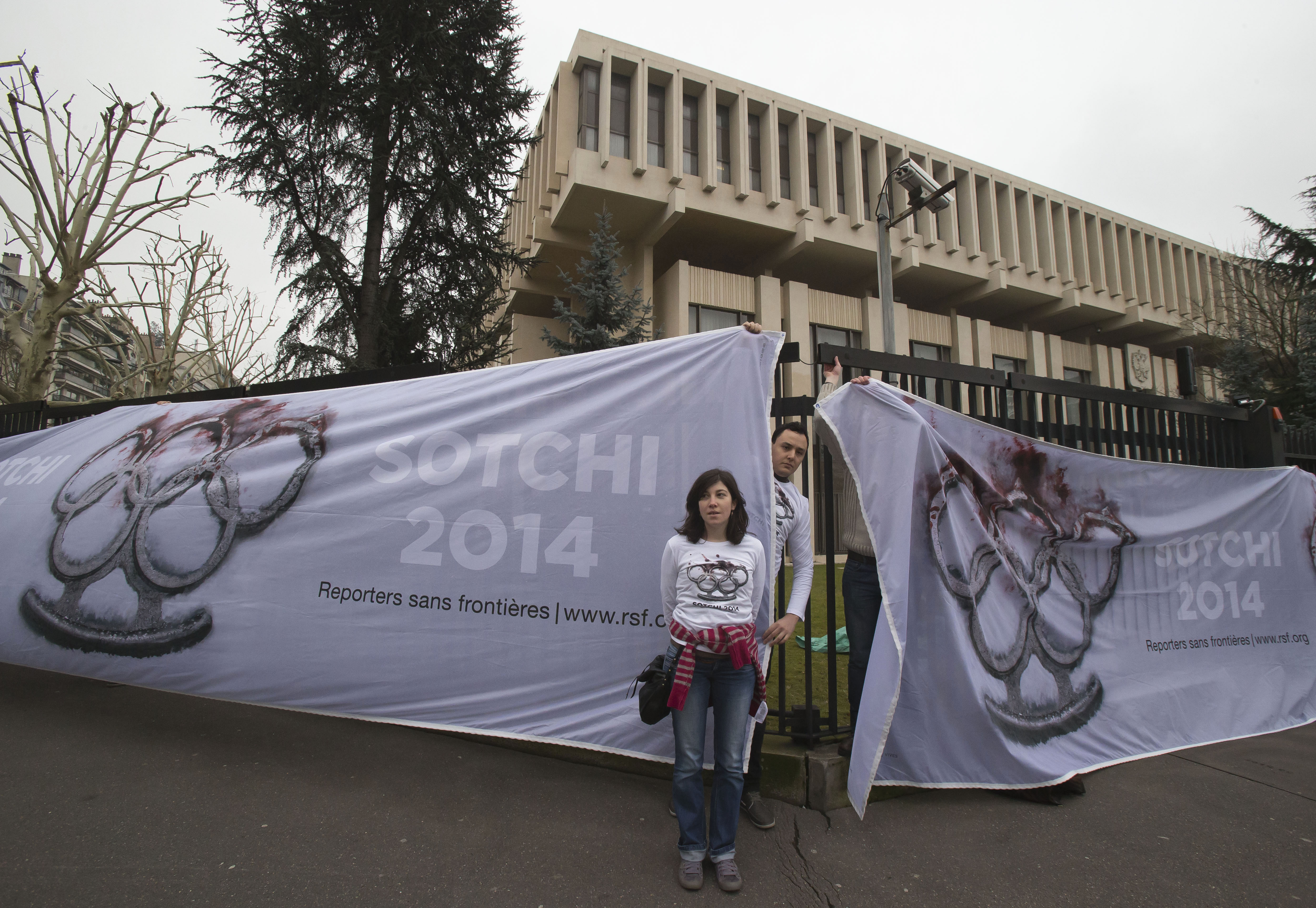 1 March 2013, France. Activists with Reporters Without Borders (RSF) stand outside of the Russian embassy in Paris in front of banners featuring blood-covered brass knuckles in the design of the Olympic rings.