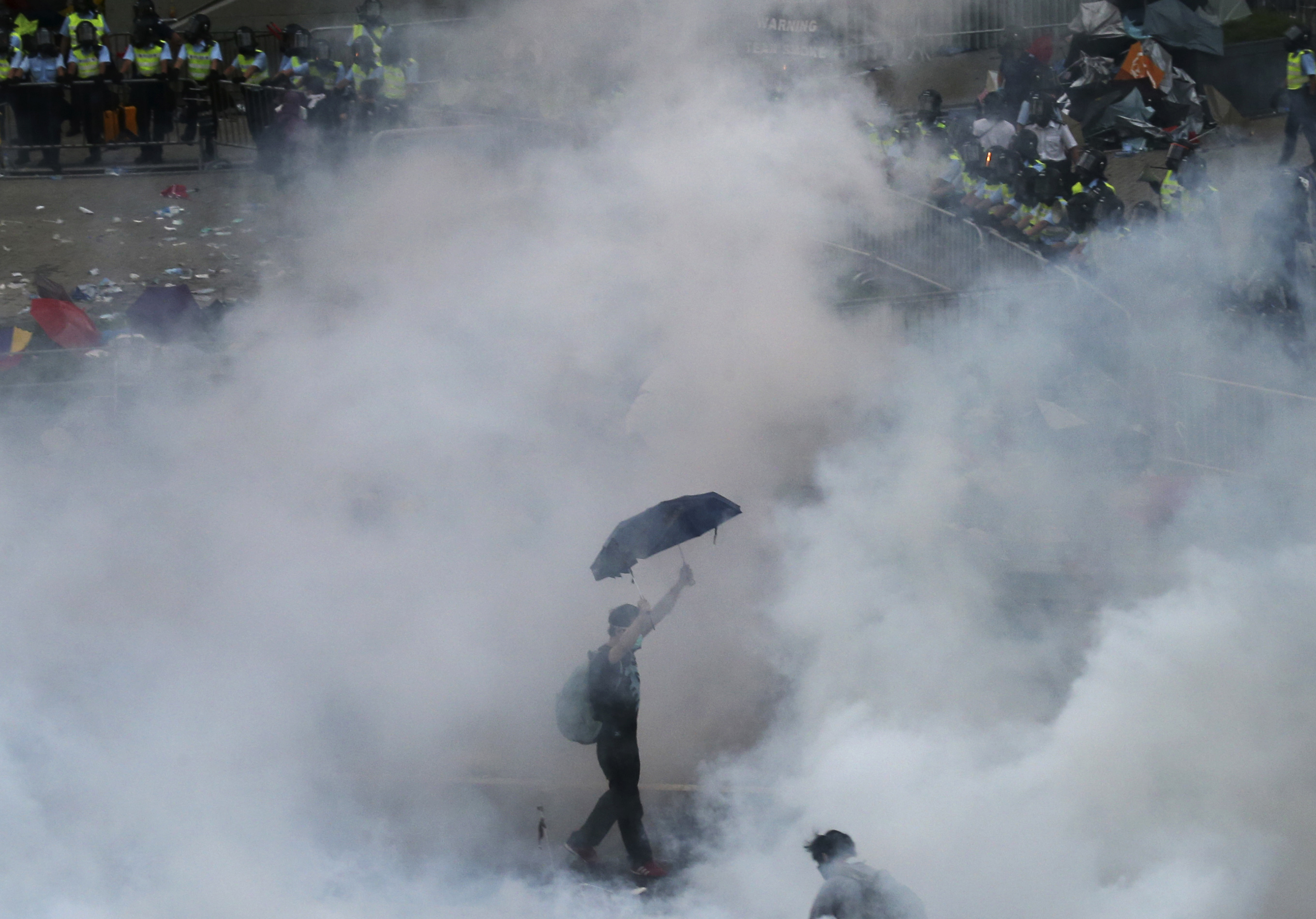 A protester walks in tear gas fired by riot policemen after thousands of protesters blocking the main street to the financial Central district outside the government headquarters in Hong Kong, 28 September 2014