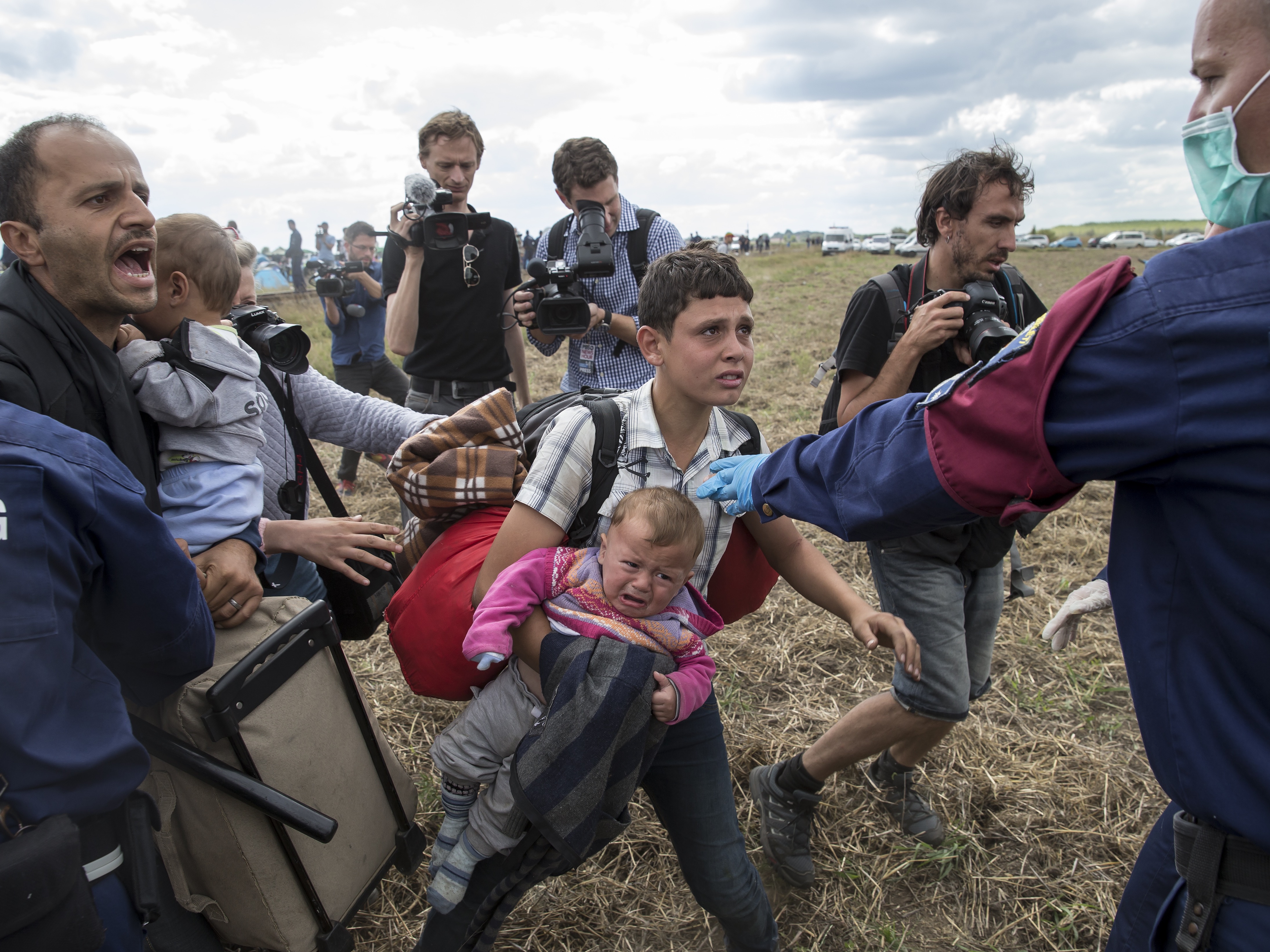 A migrant carrying a baby is stopped by Hungarian police officers as he tries to escape on a field nearby a collection point in the village of Roszke, Hungary, 8 September 2015